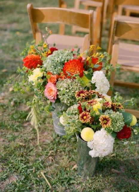 rustic floral arrangements in burgundy, red, yellow and white in buckets for a fall rustic wedding