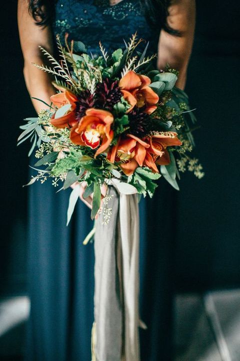 a moody wedding bouquet with textural greenery, dark plum and rust flowers plus long grey ribbons