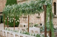 an overhead greenery decoration with white blooms and hanging candle lanterns plus a matching greeney runner