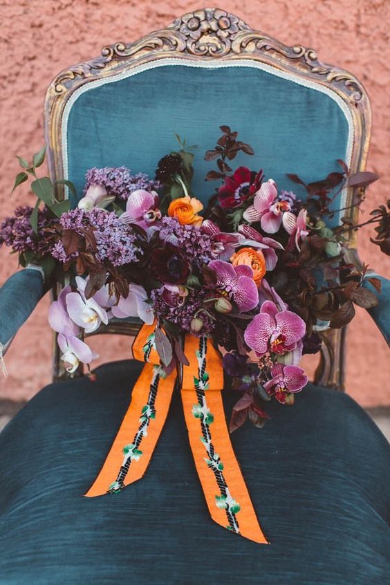 a colorful yet moody wedding bouquet with lilac, pink orchids, dark foliage and orange touches for a wow look
