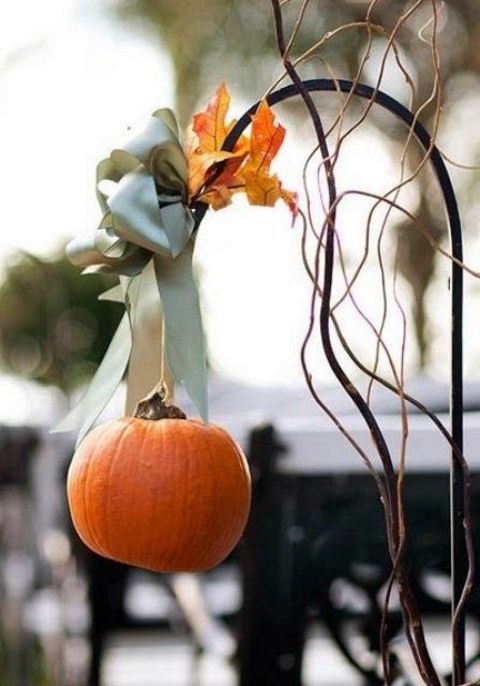 a cute little pumpkin with a green ribbon and leaves on a metal stand for a rustic feel