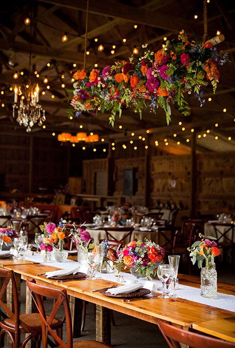 a colorful floral decoration filled with orange roses, purple dahlias and daisies for a rustic wedding