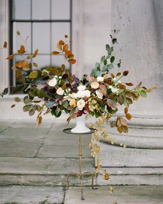 a lush fall wedding centerpiece with white blooms and fall leaves looks very natural and soft