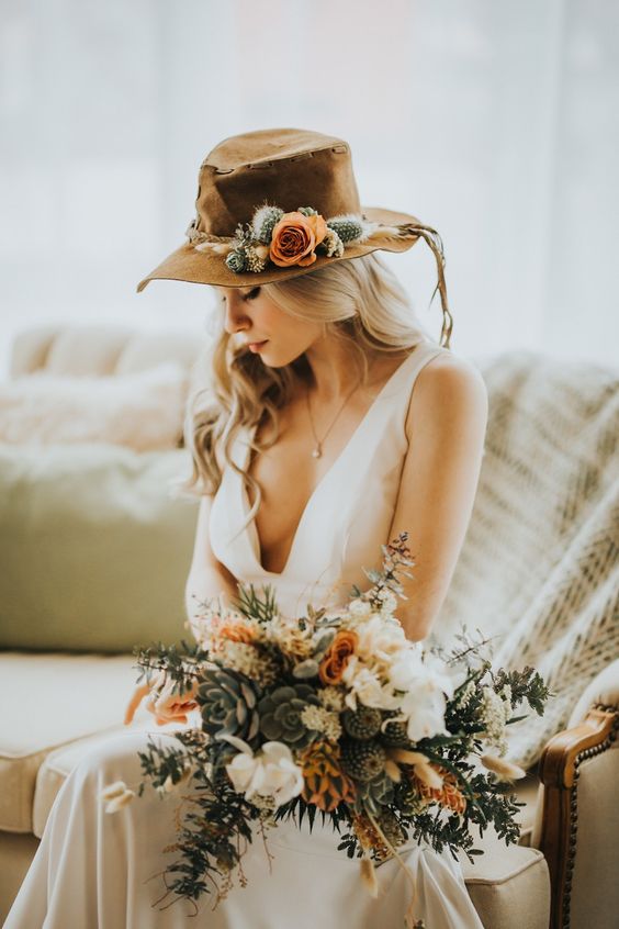 a desert-inspired bridal look with a plunging neckline wedding dress and a brown hat topped with cacti and a bloom