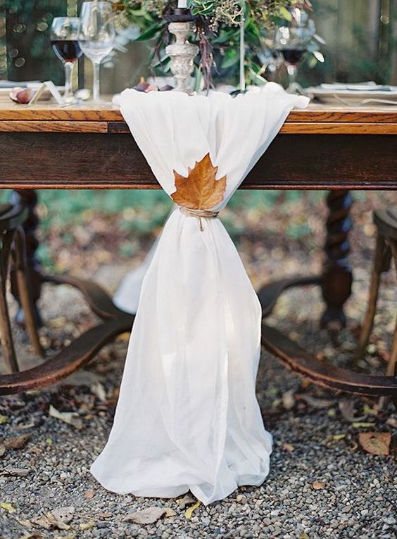 a white fabric table runner decorated with a single leaf and twine looks very refined and fall-like