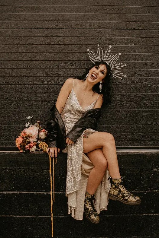 a bold and chic rock n roll bridal look with a white sequin slip wedding dress, a black leather jacket, printed boots, a sunburst headpiece and a chic bouquet