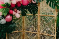 02 a boho tropical photo booth with a wicker backdrop decorated with tropical leaves and pink balloons