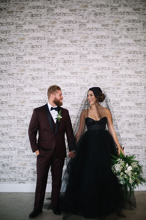 a burgundy suit with black lapels for the groom and a black wedding dress for the bride