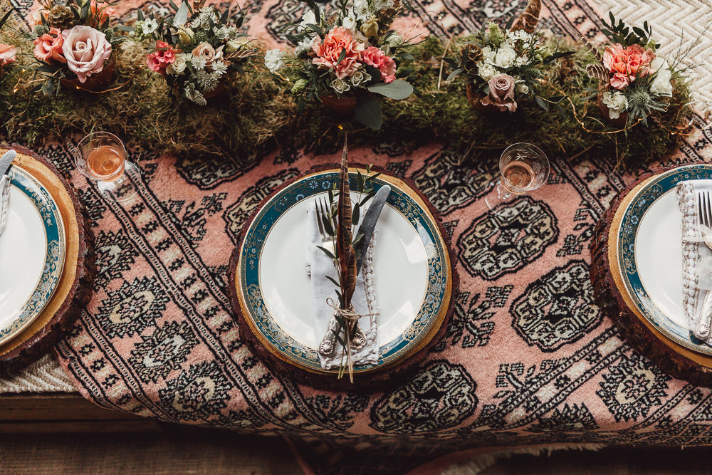 The wedding tablescape is done with boho fabric, a moss runner with blooms and wood slice chargers