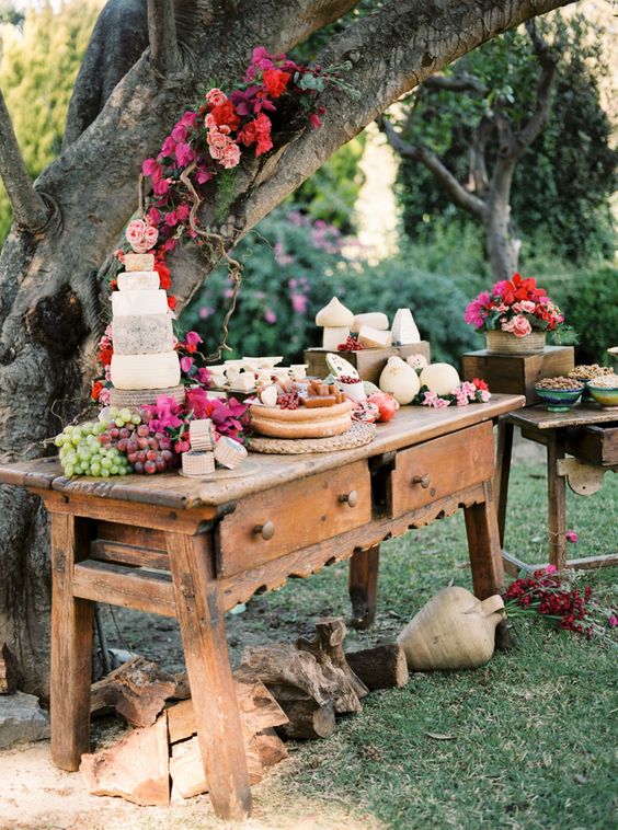 an outdoor dessert, fruit and cheese table decorated with lush and bright florals