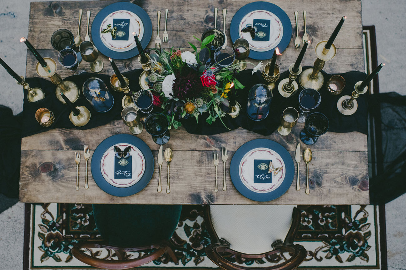 a chic tablescape with a black runner and candles, blue chargers, moody blooms and gilded touches
