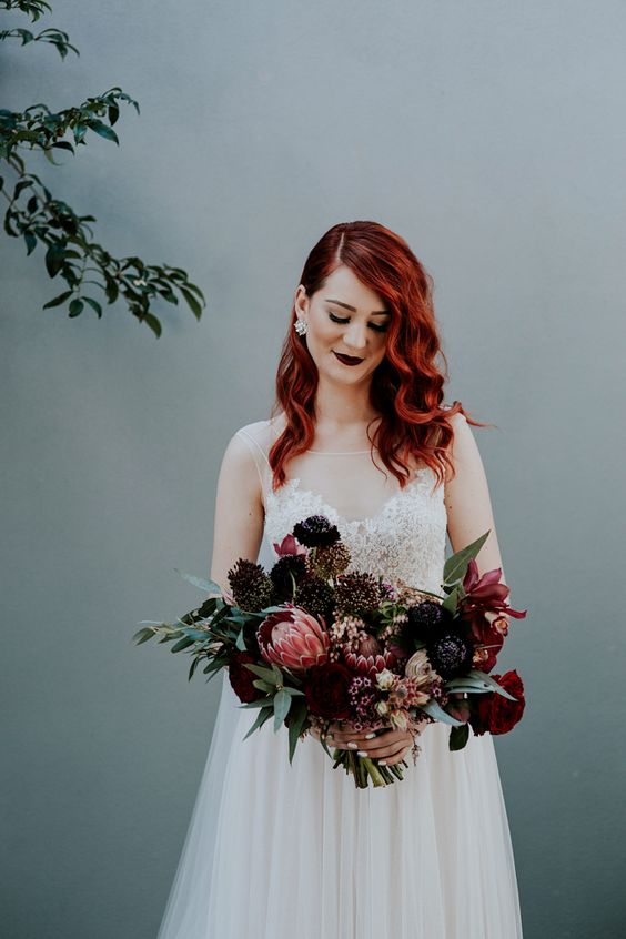 a burgundy and black wedding bouquet with greenery and a matching dark bridal lip