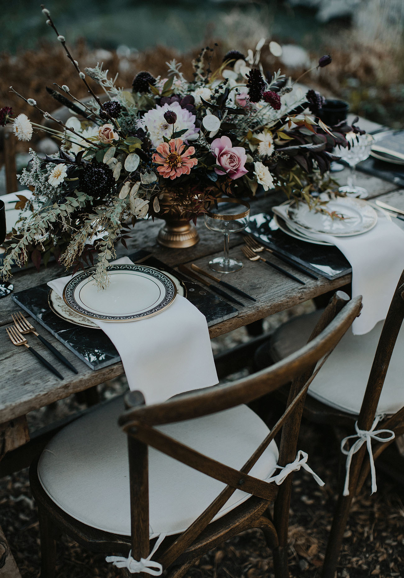 A gorgeous haunted tablescape with a lush textural centerpiece, marble chargers, printed plates, gilded touches and white napkins