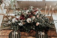 15 a haunted table setting with a lush floral centerpiece, off-white candles, black cahrgers and a grey table runner