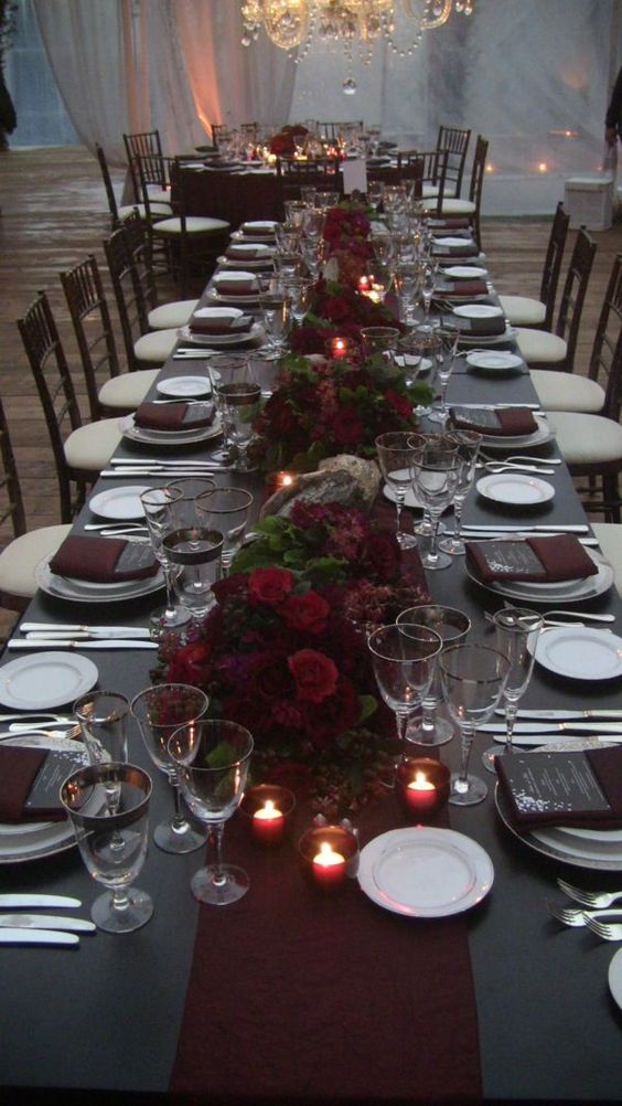 a moody tablescape with a black tablecloth, black menus, burgundy napkins and floral centerpieces
