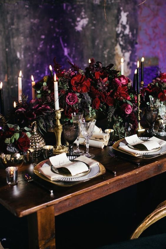 a luxurious table setting with a lush dark floral centerpiece, black and white candles, gilded touches for elegance