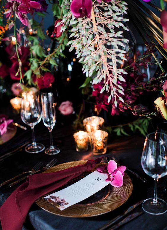 a burgundy and black tablescape with hanging florals and candles for a luxurious wedding