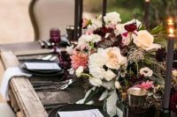 23 a moody haunted wedding tablescape with an uncovered table with a moody floral centerpiece, black candles and chargers and colored glasses