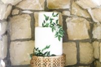 24 a simple whie cake with greenery on an elegant metallic stand is a stylish combo