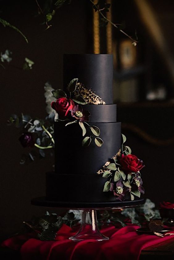 a matte black wedding cake with a touch of gold and sugar burgundy blooms and greenery