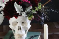 25 a stack of books, a skull with a dark floral arrangement with dark burgundy florals, pale and saturated greenery and berries
