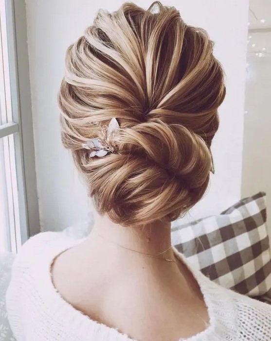 a chic and voluminous bridal chignon hairstyle with a wavy bump on top and a little floral hairpiece