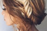 a messy and wavy updo with a large fishtail braid in the center and locks down