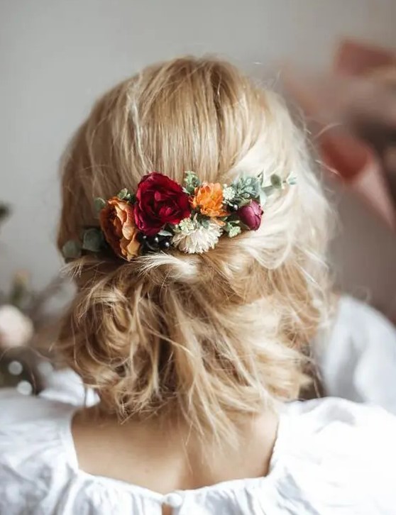 a messy low updo with textural hair and bright fall blooms and greenery is a gerat idea for both fall and summer weddings