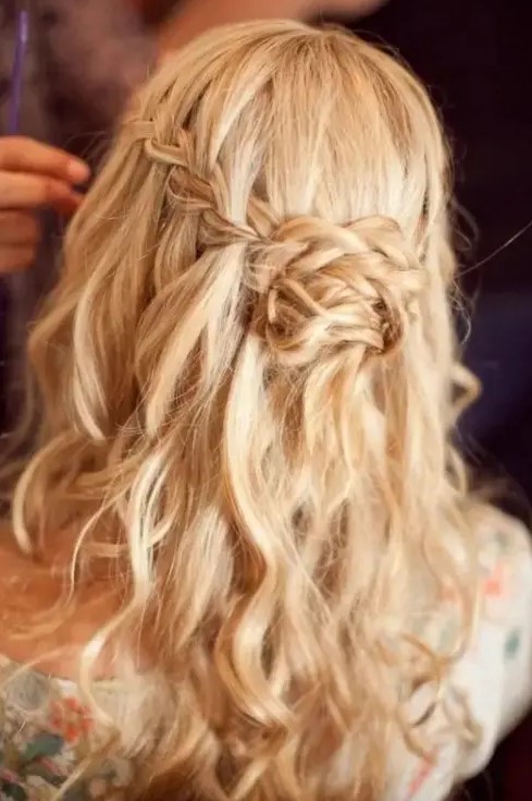 a messy wavy half updo with a braided halo and a braided knot for a relaxed and boho look
