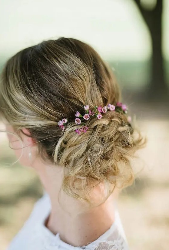 a textural messy updo with braids, a bump and little flowers to add a touch of color for a bride or bridesmaid look