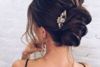 a very messy wavy twisted chignon with some locks down and a large rhinestone hairpiece for a sexy look