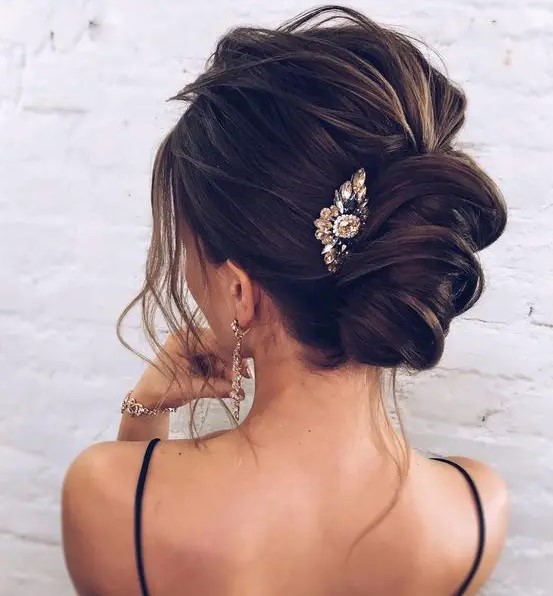 a very messy wavy twisted chignon with some locks down and a large rhinestone hairpiece for a sexy look