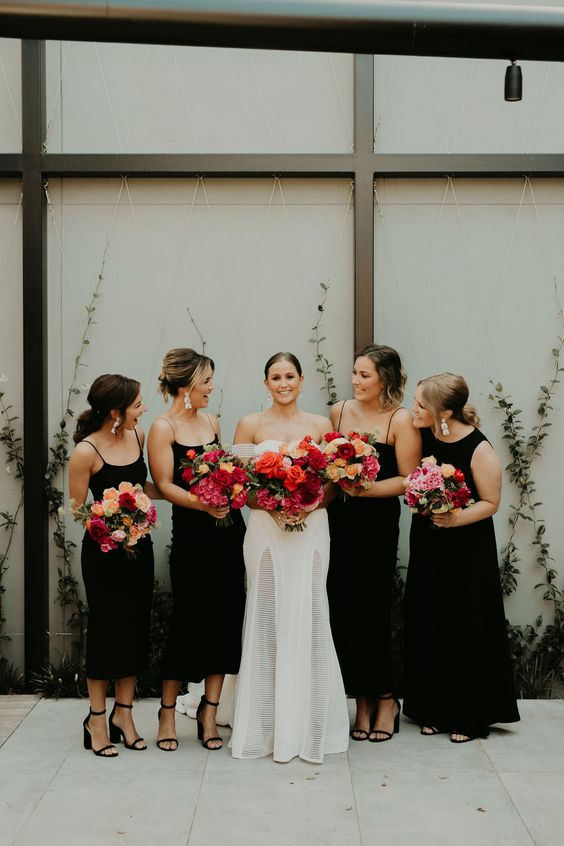 matching black midi bridesmaid dresses with spaghetti straps and a maid of honor in a maxi A line dress with no sleeves