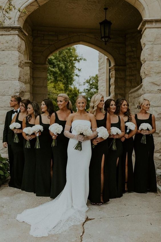 stylish matching black maxi bridesmaid dresses with thick straps and square necklines and thigh high slits for a modern formal wedding