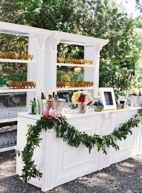 a sweet backyard cocktail bar decorated with a greenery garland and spruced up with colorful glasses
