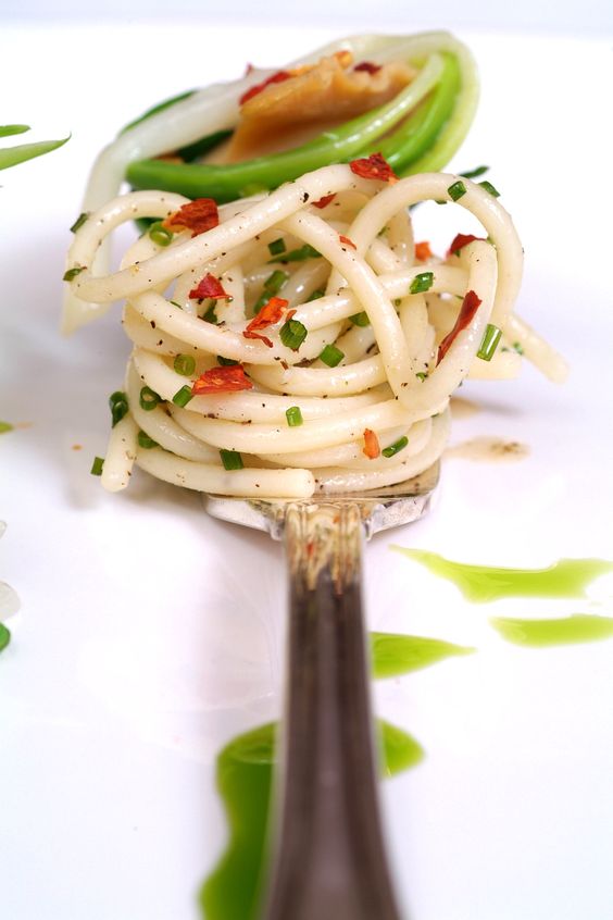 a bite-sized appetizer of noodles on a fork and some greenery