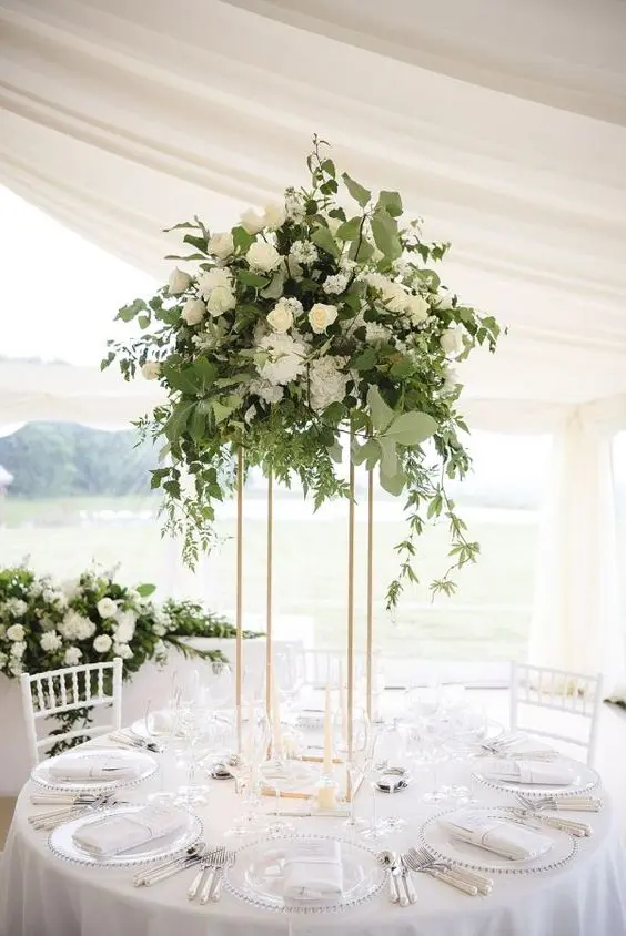 a chic eucalyptus, olive branch and white bloom centerpiece on a tall gold stand