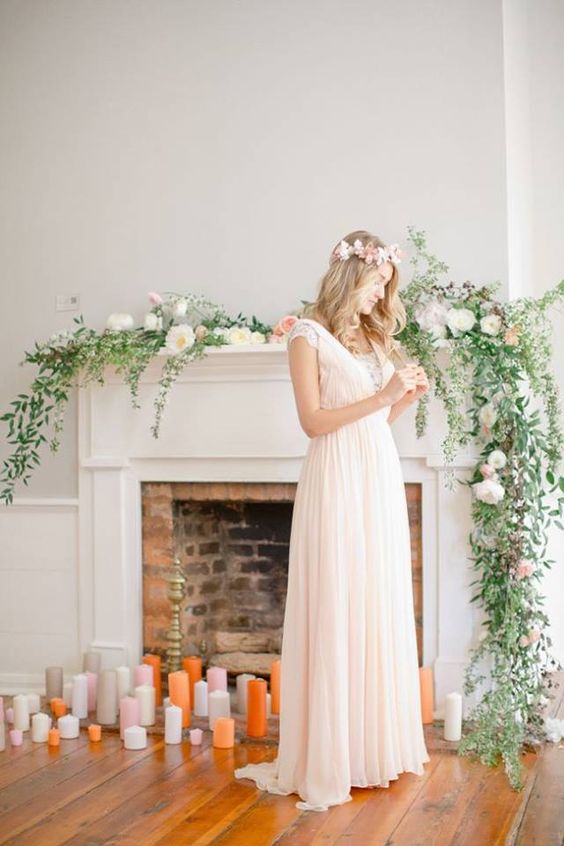 a chic fireplace backdrop with colroful candles on the floor and a greenery and floral garland on the mantel