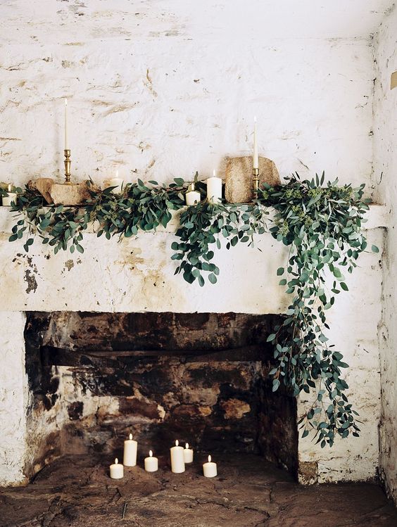 a chic fireplace with candles inside and on the mantel, with cascading greenery and stones