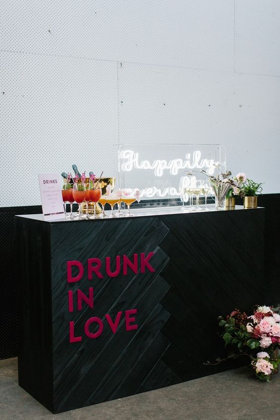 an ultra-modern wedding cocktail bar with an acrylic calligraphy sign, blooms and pink letters