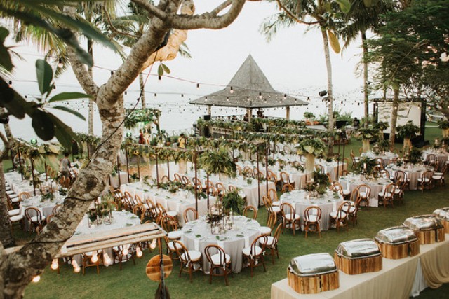 The wedding reception was outdoors, with lots of lights and much greenery over the tables