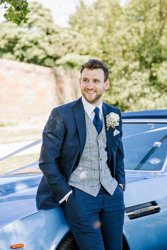 a navy suit with a grey checked waistcoat and a navy tie plus a lush white floral boutonniere