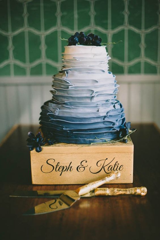 an ombre white to navy ruffle wedding cake topped with berries and dark blooms