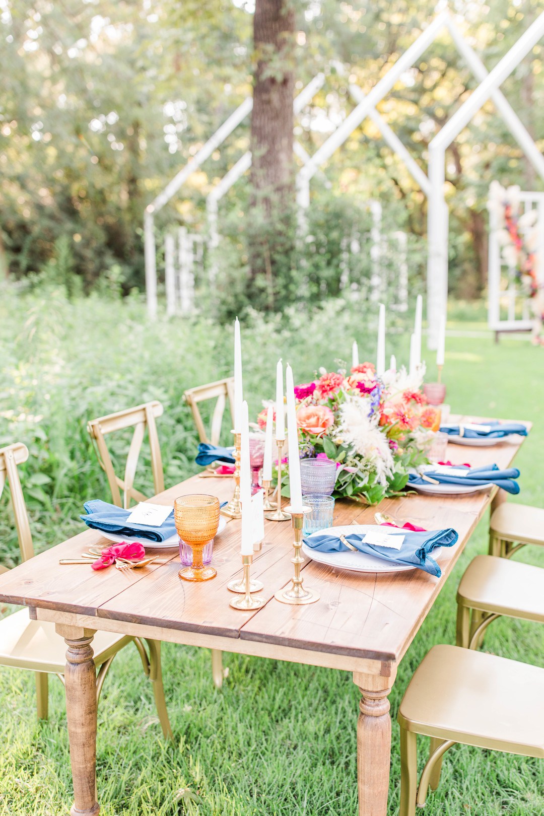 The wedding tablescape was done with blue napkins, pink bows, gilded touches and colored glasses plus lush florals