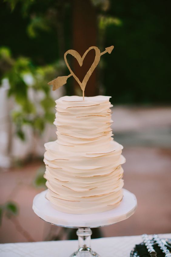 a chic white ruffle wedding cake with gold edges and a simple gold heart topper is a cute idea