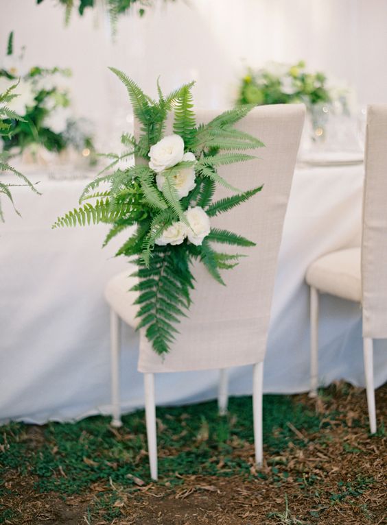 a fabric covered chair decorated with ferns and white blooms is a creative idea