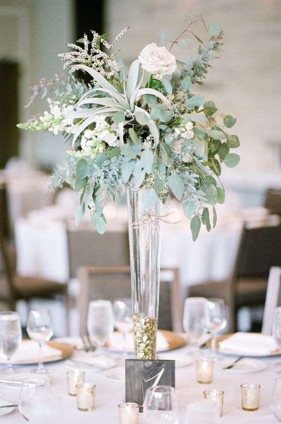 a modern tall centerpiece with a tall gold foil vase, eucalyptus, bluhs roses, herbs and air plants