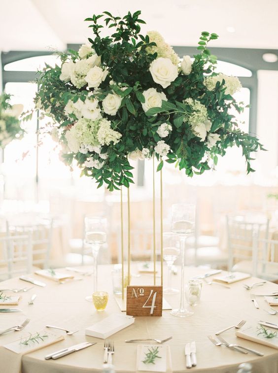 a stylish wedding centerpiece of white roses and hydrangeas and textural greenery on a tall thin stand