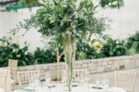 15 a tall and airy centerpiece of foliage and white blooms in a clear vase looks very chic and elegant