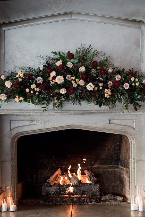 a vintage fireplace with candles, a real fire and a very lush floral decoration with greenery